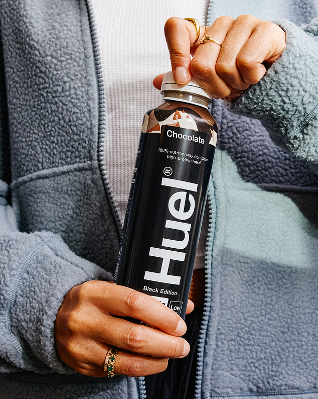 Lifestyle photography of a consumer holding a Huel Black Edition chocolate meal replacement bottle, representing the efficiency-driven marketing funnel used by subscription-based health and nutrition brands.